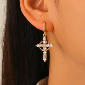 Close-up of golden cross earrings with white cubic zirconia on a female model