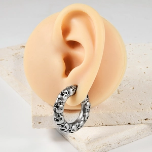 Close-up of silver skull embossed ear tunnels on model with textured stone background