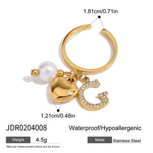 Détail d'une bague en acier doré 18K avec perle, cœur et charms lettre G en cristal