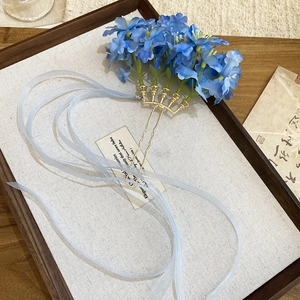 Detail of fabric flower hair pin with light blue ribbons on wooden tray