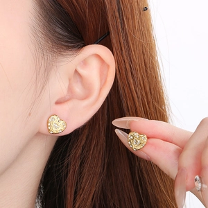 Macro shot of gold heart-shaped stud earring featuring intricate textures and white diamonds