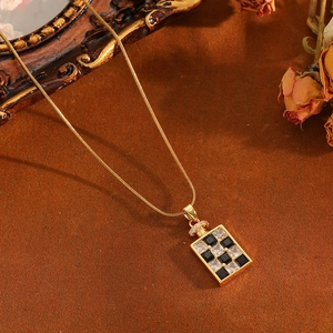 Detail view of the gold checkered pendant necklace on a vintage background with snake chain