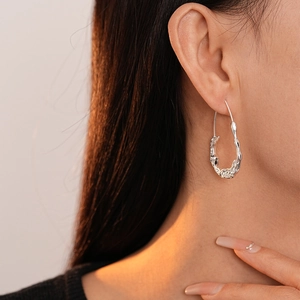 Close-up of liquid metal style silver oval hoop earrings worn on female model's ear