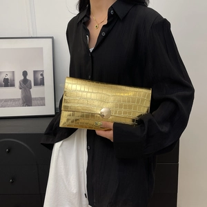 Detail of gold clutch bag featuring crocodile texture and large circular metal buckle
