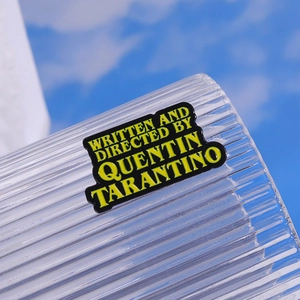 Quentin Tarantino movie brooch with yellow text on black enamel and blue sky background