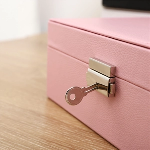 Detail of a pink PU leather jewelry box featuring a silver metal lock and key on a wood surface