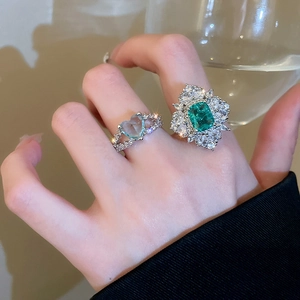 Macro detail of double-layer zircon heart ring with emerald-cut green gemstone and silver finish