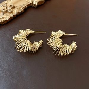 Detailed view of hollow gold-plated twisted C-shaped earrings on brown leather