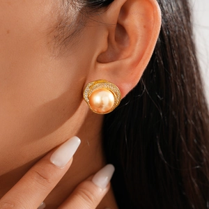 Macro detail of champagne pearl earrings with gold-plated zircon settings on a model
