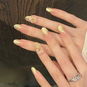 Golden glitter gradient almond press-on nails with 3D white floral accents and crystals