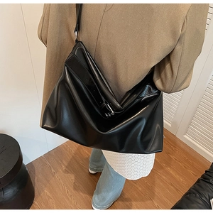 Gros plan d'un sac cabas en cuir PU noir brillant avec bandoulière et boucle métal