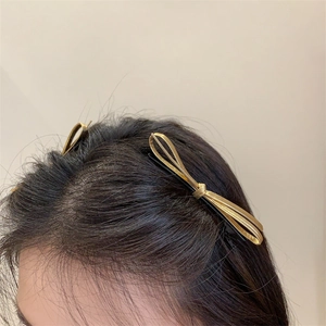 Close-up of a minimalist golden metallic bow hair clip styled on hair side