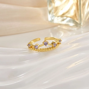 Detail of a golden crown ring featuring five purple gemstones on a white silk background