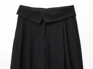 Detail view of black high-waisted trousers featuring a cross-waist design and frayed edges