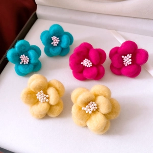 Detailed macro of wool felt flower earrings with white beads in blue, pink, and yellow