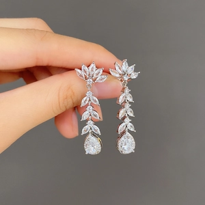 Silver long tassel zircon earrings with pear-shaped drops shown on hand against beige background
