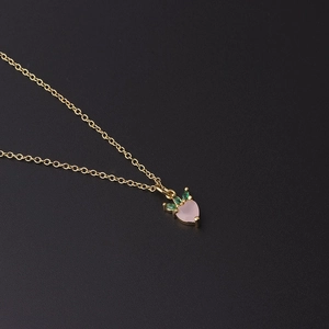 Detailed close-up of a gold strawberry pendant necklace with pink and green zircon stones