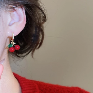 Close-up of red zircon cherry stud earrings with gold metal leaf and diamond accents