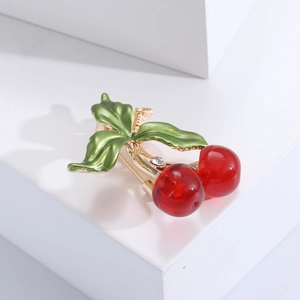 Broche cerise à la mode avec boules rouges et feuilles émaillées vertes sur fond blanc