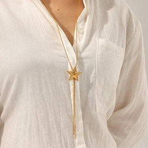 Long gold pentagram star pendant necklace with fringe tassel worn over a white shirt