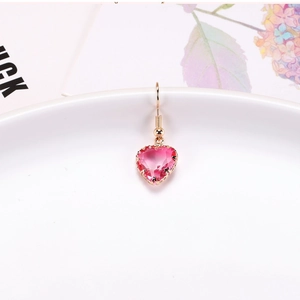 Close-up of pink heart-shaped crystal earring with gold-plated setting and hook on white plate