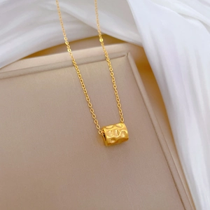 Detailed close-up of a gold hammered cylinder pendant on a titanium steel necklace