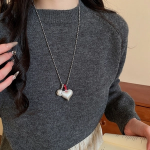 Close-up of double heart pendants on a silver ball chain worn with a cozy grey sweater