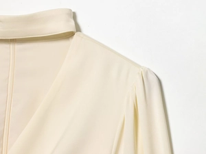 Dettaglio dell'elegante camicia in raso crema con scollo a V e pieghe sulle spalle della maglia