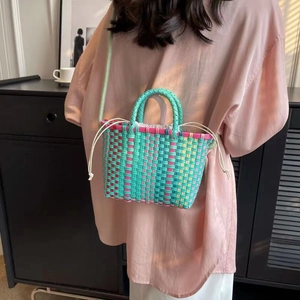 Detail of colorful woven bucket bag with drawstring closure and crossbody strap on model