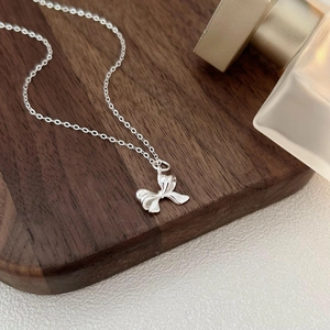 925 sterling silver bow pendant necklace with slim chain on a dark walnut wood surface