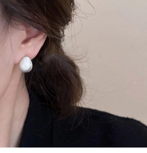 Close-up of a silver matte teardrop earring worn by a model for a minimalist aesthetic