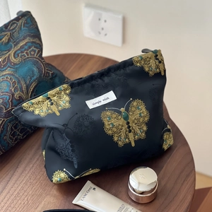 Elegant black cosmetic bag with golden butterfly embroidery and beaded details on wood table