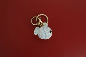 Detail of handmade light blue and white striped crochet clownfish keychain on red backdrop
