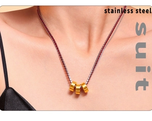 Close-up of three gold-plated stainless steel cylinder charms on a red zircon chain