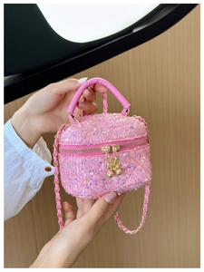 Close-up of pink sequin handbag with gold chain strap and bell detail on fabric