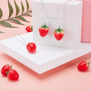 DIY resin strawberry pendant jewelry set with silver necklace and earrings on pink display