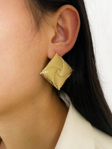 Close-up of golden geometric square earrings with textured swirl pattern on model