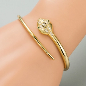 Detailed view of a gold snake wrap bracelet with white crystals and green gemstone eyes
