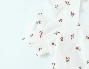 Detailaufnahme von weißem Kleid mit rotem Rosenmuster und Puffärmeln mit Gummiband