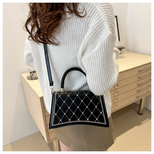 Detail of black quilted handbag with white diamond pattern and woven top handle on a model