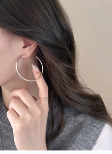 Close-up of a model wearing large silver C-shaped hoop earrings with a minimalist design