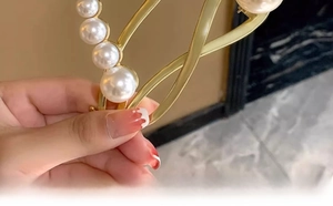 Detail showing five white pearls on a gold alloy hair claw clip held by hand
