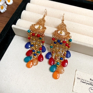 Detail shot of vintage Bohemian tassel earrings with colorful beads on a beige velvet surface