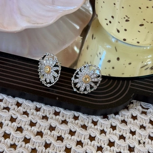 Detailed close-up of silver daisy stud earrings with yellow gemstone and pavé diamonds