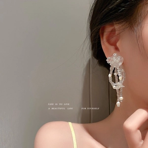 Detail of drop earrings featuring white petals, clear beads, and small pearls on model