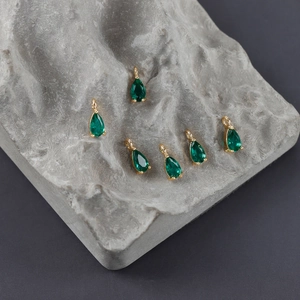 Detalle macro de seis colgantes de gota verde esmeralda con engaste de circón chapado en oro 18k