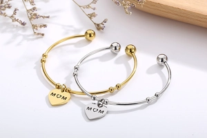 Vue détaillée des bracelets à breloque cœur MOM or et argent sur un plateau en bois fleuri