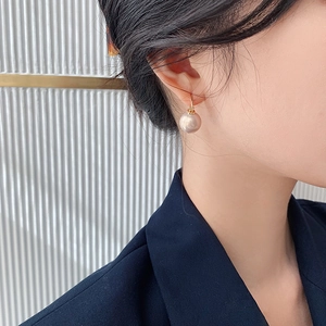 Close-up of elegant champagne pearl earrings with gold hooks on a female model