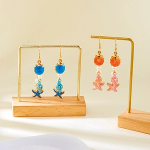 Detailed macro of ocean-themed shell and starfish drop earrings with hanging pearls