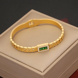 Macro detail of gold stainless steel bracelet featuring green gemstones and cubic zirconia